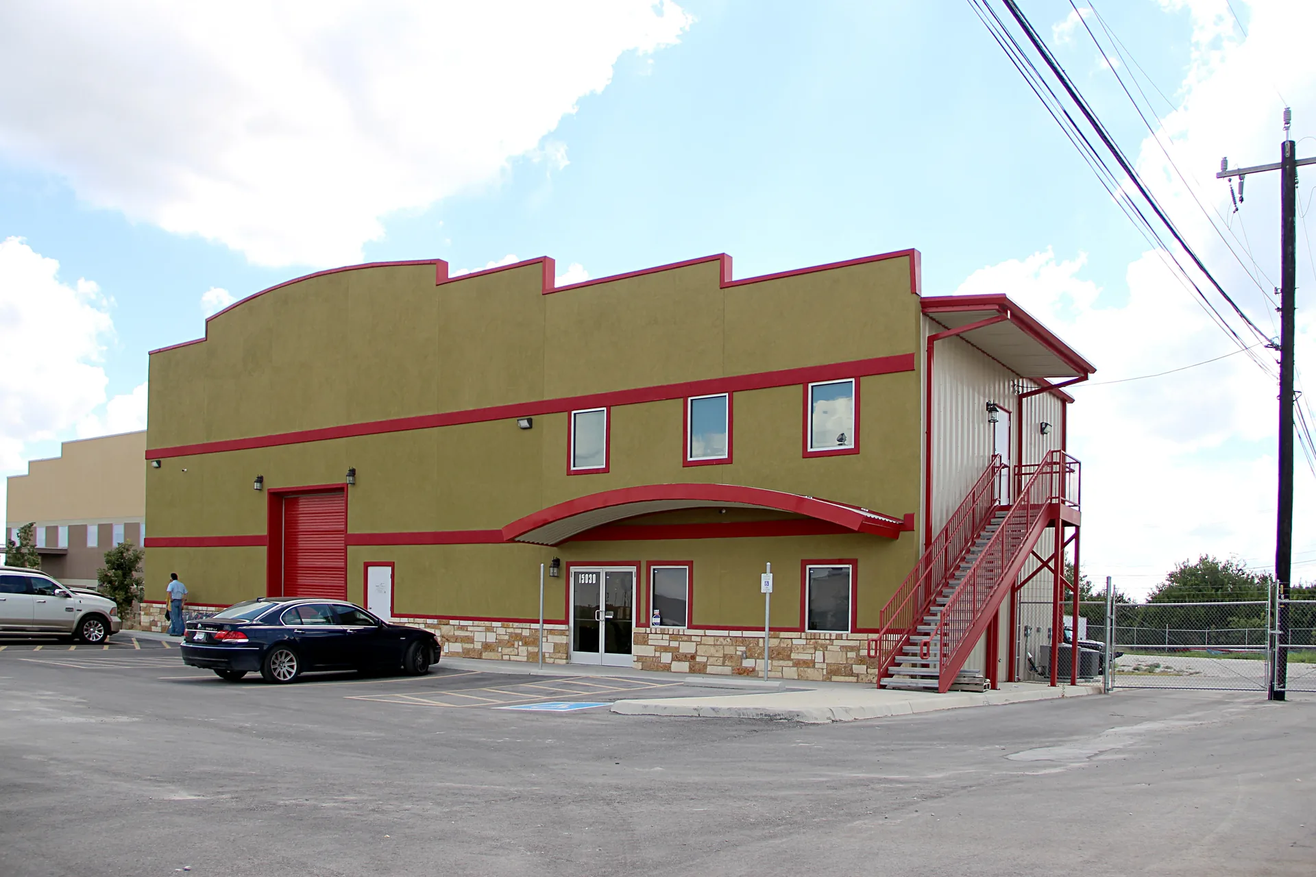 Finished two-storey commercial metal building faced in stucco with red trim and an exterior steel stair